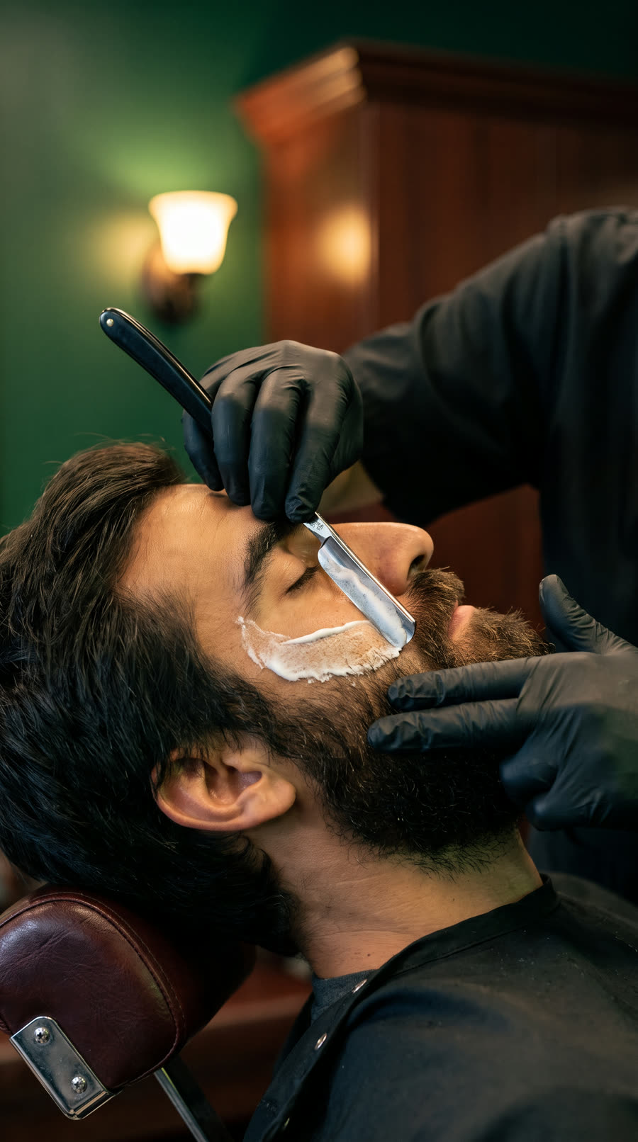 Barber shaving a client's cheek with a straight razor